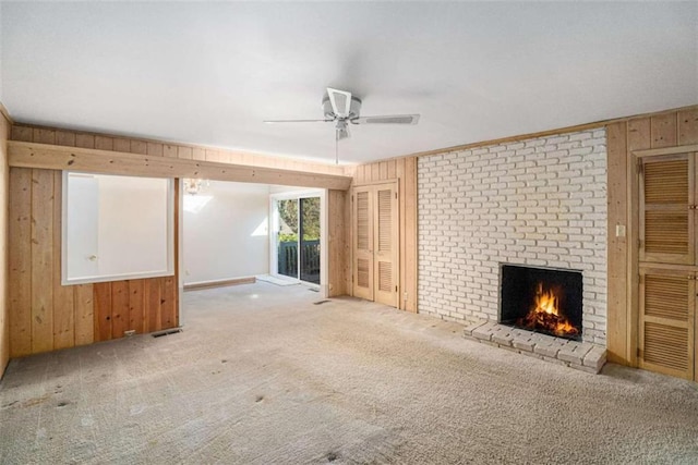 unfurnished living room featuring ceiling fan, carpet floors, wooden walls, and a fireplace