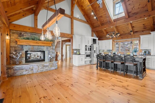 living room featuring beamed ceiling, a fireplace, high vaulted ceiling, wooden ceiling, and light hardwood / wood-style flooring