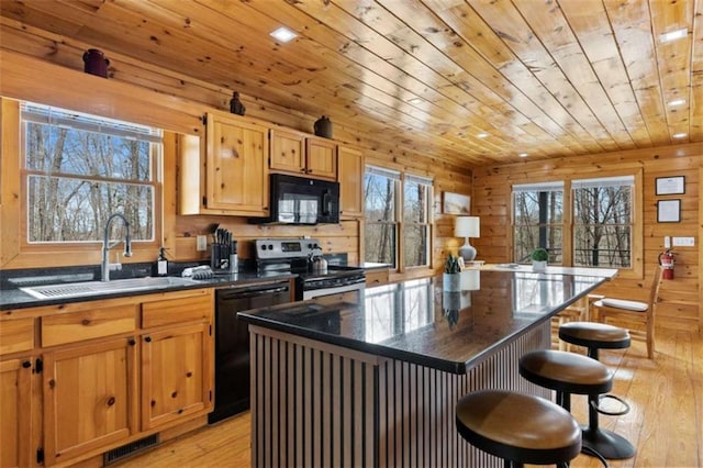 kitchen with black appliances, a sink, wooden ceiling, a breakfast bar, and light wood-style flooring