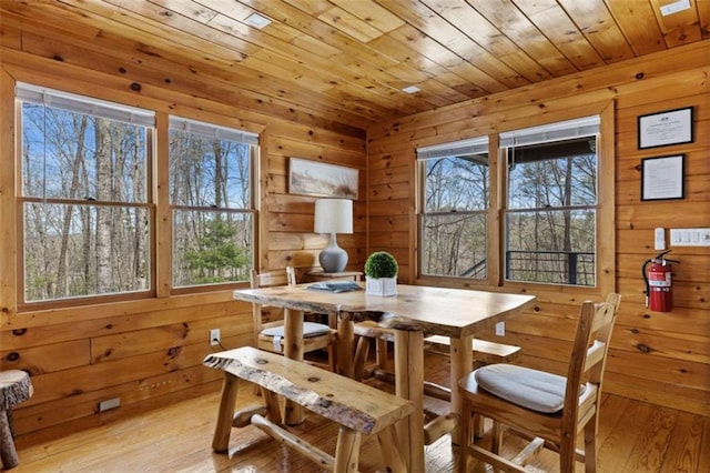 dining area with wood walls, wood ceiling, light wood-type flooring, and healthy amount of natural light