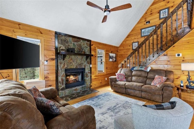 living room featuring wood walls, wood finished floors, stairs, a ceiling fan, and a fireplace