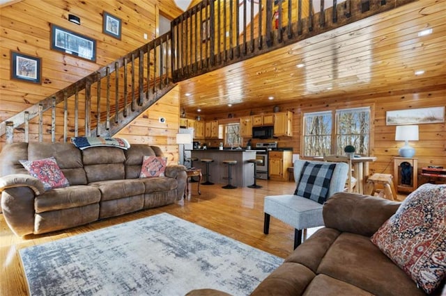 living area featuring wood walls, light wood-type flooring, a high ceiling, stairs, and recessed lighting