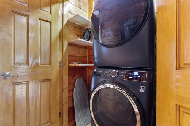 laundry room featuring stacked washing machine and dryer and wood walls
