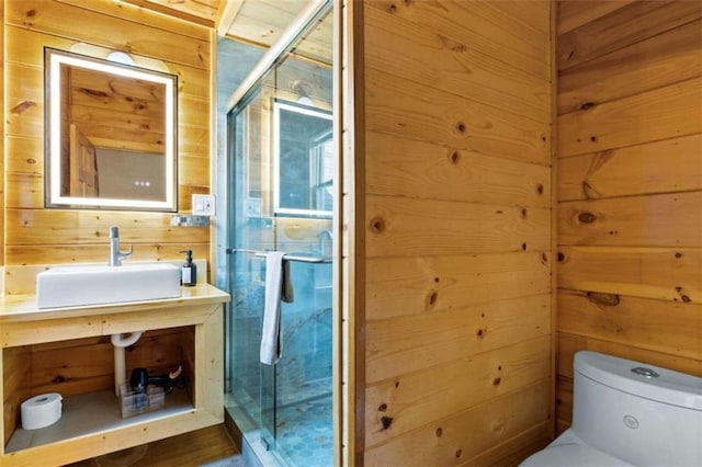 bathroom featuring a sink, toilet, wooden walls, and a shower stall