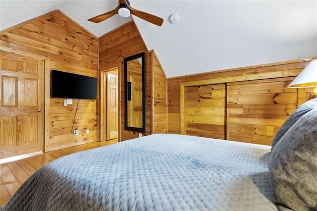 bedroom featuring lofted ceiling, wood walls, wood finished floors, and a ceiling fan