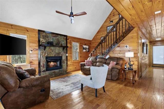 living room featuring wood-type flooring, wood walls, ceiling fan, a stone fireplace, and vaulted ceiling