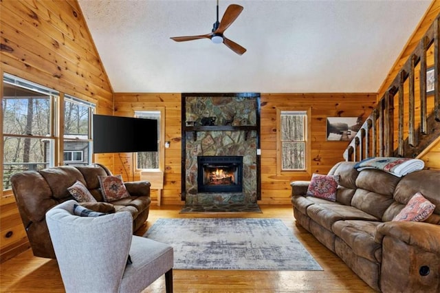 living area featuring vaulted ceiling, wood walls, ceiling fan, a fireplace, and wood finished floors