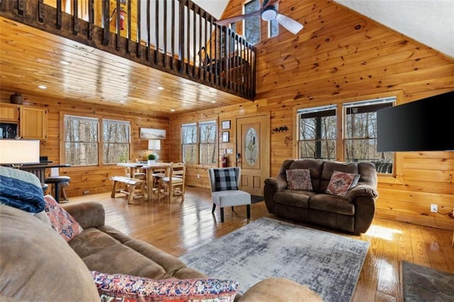living room with hardwood / wood-style floors, wooden walls, a ceiling fan, recessed lighting, and a towering ceiling
