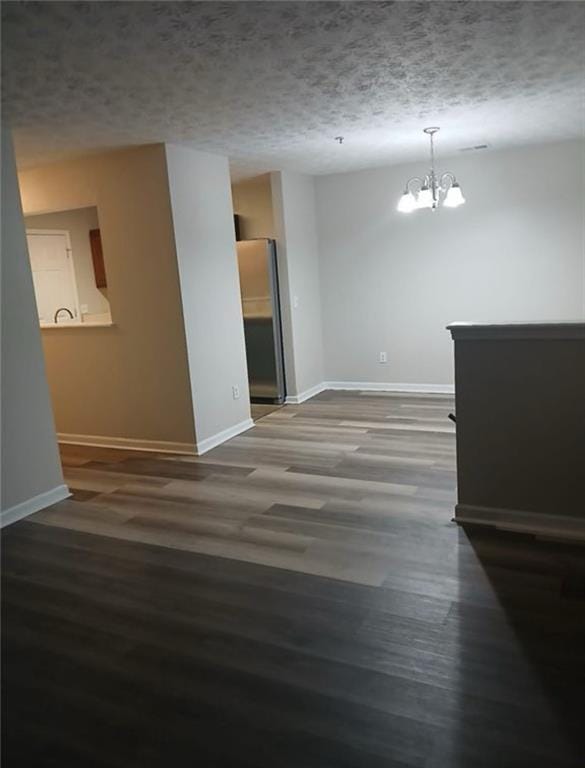 empty room with a textured ceiling, dark hardwood / wood-style floors, and an inviting chandelier