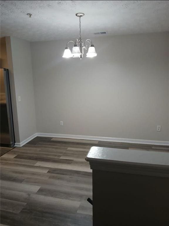 spare room with dark hardwood / wood-style floors, an inviting chandelier, and a textured ceiling