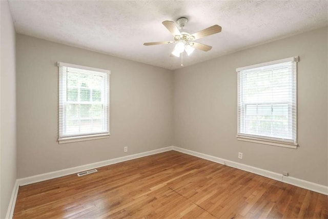 spare room with a textured ceiling, a wealth of natural light, hardwood / wood-style floors, and ceiling fan