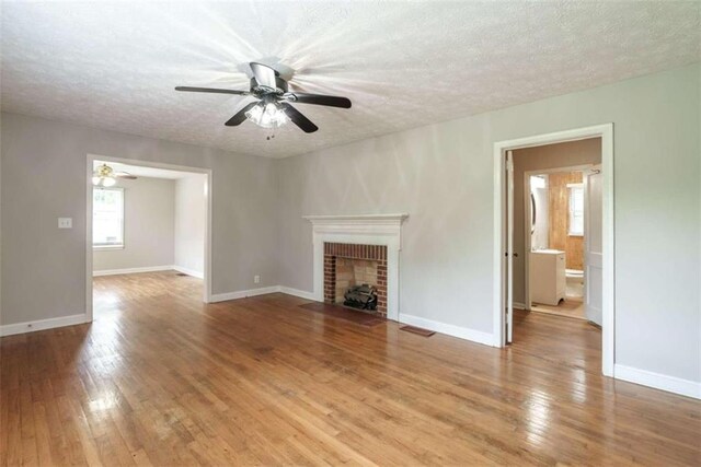 unfurnished living room with hardwood / wood-style floors, ceiling fan, a fireplace, and a textured ceiling