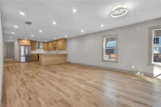 kitchen featuring light wood-type flooring, wall chimney exhaust hood, stainless steel fridge, kitchen peninsula, and tasteful backsplash