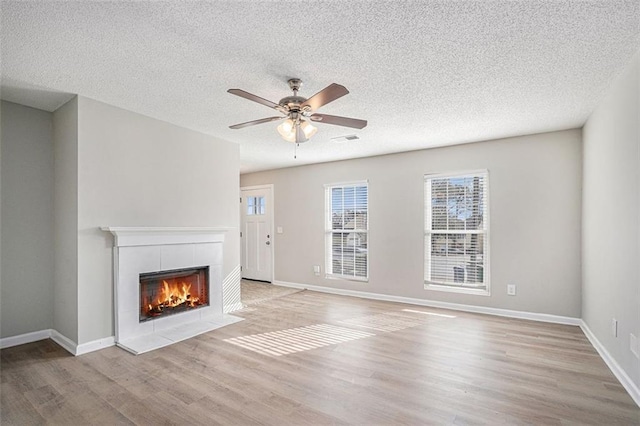 unfurnished living room featuring a textured ceiling, a fireplace, ceiling fan, and light hardwood / wood-style floors