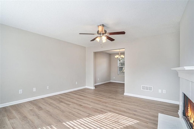 unfurnished living room with light hardwood / wood-style floors, a textured ceiling, and ceiling fan with notable chandelier