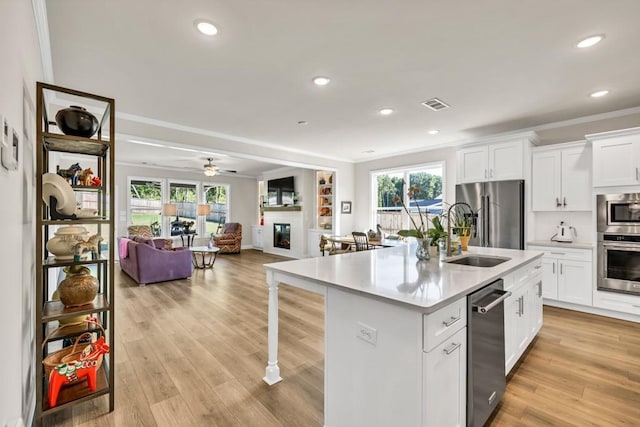 259 Dunagan Ct, Winder, GA 30680 - kitchen featuring appliances with stainless steel finishes, a glass covered fireplace, open floor plan, a kitchen island with sink, and light countertops