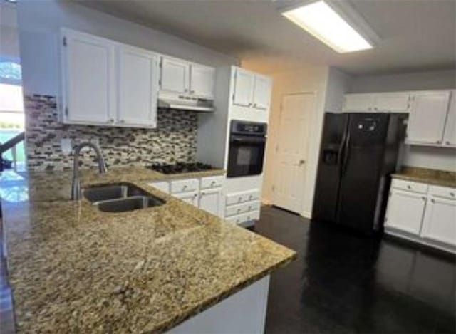 kitchen featuring light stone counters, a sink, black appliances, exhaust hood, and a peninsula