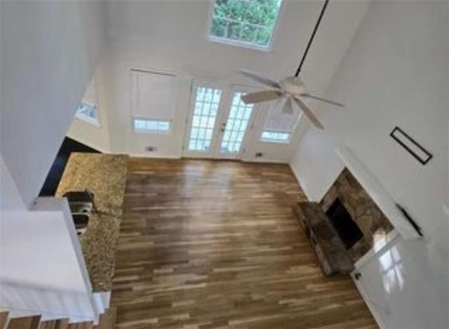 unfurnished living room with wood finished floors, a ceiling fan, a towering ceiling, and a fireplace with raised hearth