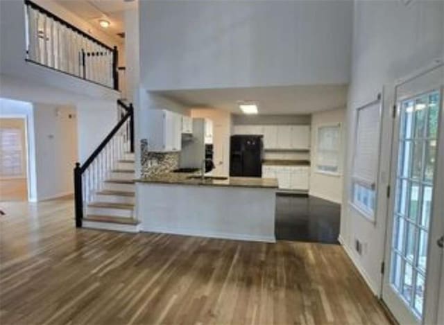 kitchen with white cabinets, a peninsula, dark wood-style floors, a towering ceiling, and refrigerator