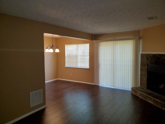 unfurnished living room featuring a stone fireplace, an inviting chandelier, a textured ceiling, and hardwood / wood-style floors