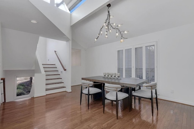 dining area with high vaulted ceiling, hardwood / wood-style flooring, a skylight, and a notable chandelier