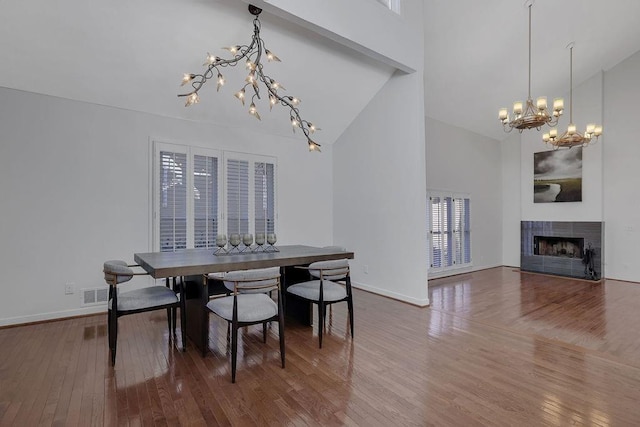 dining area featuring high vaulted ceiling, wood-type flooring, an inviting chandelier, and a tile fireplace