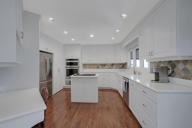 kitchen with stainless steel appliances, white cabinetry, sink, wood-type flooring, and a kitchen island