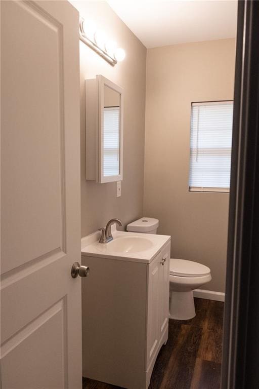 half bathroom with toilet, wood finished floors, and vanity