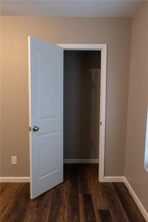 unfurnished bedroom featuring a closet, dark wood-style flooring, and baseboards