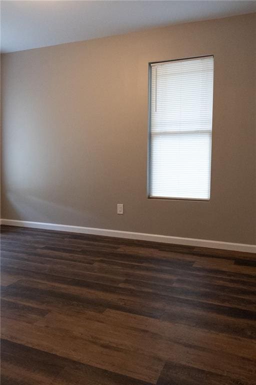 unfurnished room featuring baseboards and dark wood-type flooring