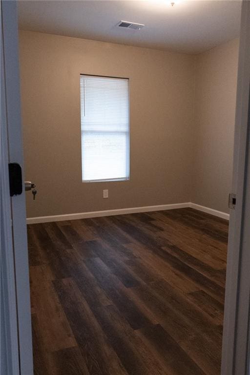 spare room with dark wood-style floors, visible vents, and baseboards