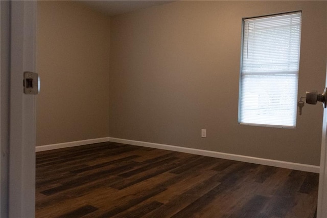 spare room with baseboards and dark wood-type flooring