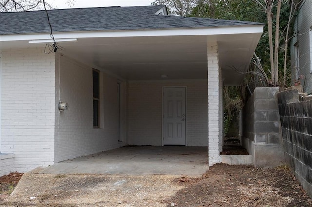 property entrance with an attached carport, roof with shingles, brick siding, and fence