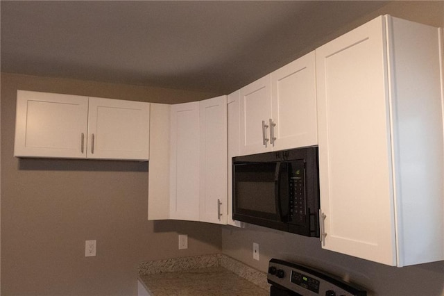 kitchen featuring black microwave, white cabinetry, and stove