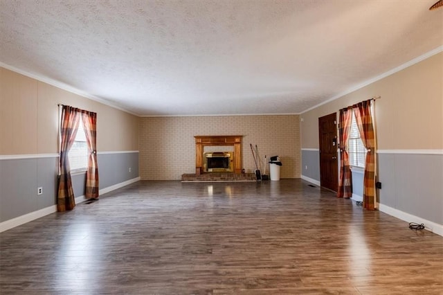 unfurnished living room featuring crown molding, dark hardwood / wood-style flooring, a brick fireplace, and a textured ceiling