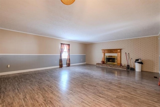 unfurnished living room featuring crown molding, brick wall, a fireplace, and dark hardwood / wood-style flooring