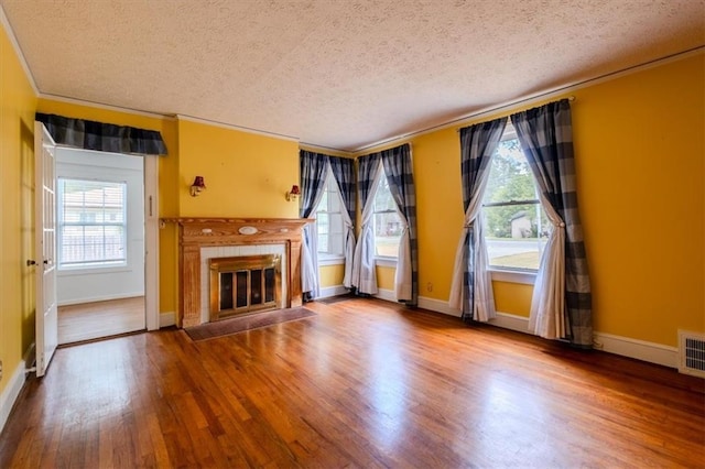 unfurnished living room featuring a healthy amount of sunlight, hardwood / wood-style floors, ornamental molding, and a textured ceiling