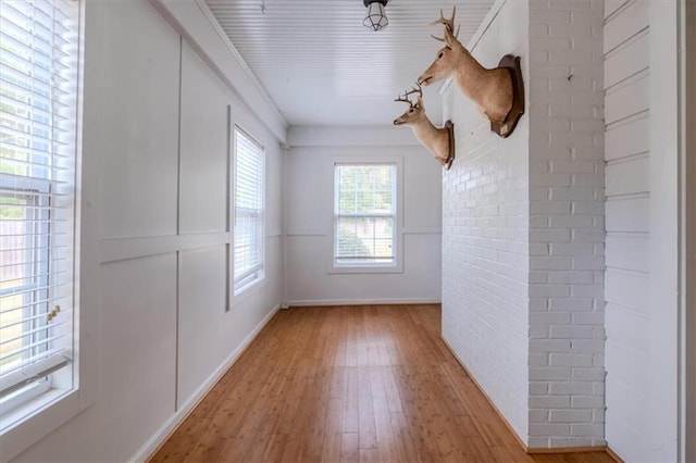 empty room with crown molding, light hardwood / wood-style floors, and brick wall