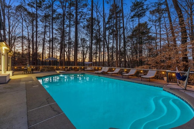 pool at dusk featuring a diving board and a patio