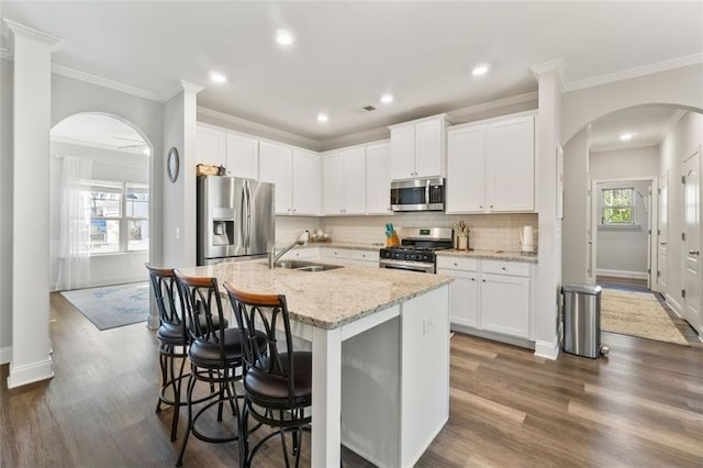 kitchen featuring tasteful backsplash, arched walkways, appliances with stainless steel finishes, an island with sink, and a sink