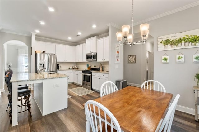 kitchen featuring arched walkways, crown molding, stainless steel appliances, and a notable chandelier