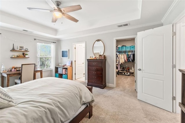bedroom featuring light carpet, a tray ceiling, a walk in closet, and visible vents