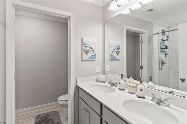 bathroom featuring toilet, crown molding, tiled shower, and a sink