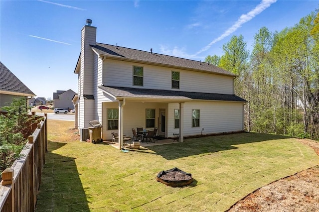 back of property with fence, a chimney, a fire pit, a yard, and a patio area
