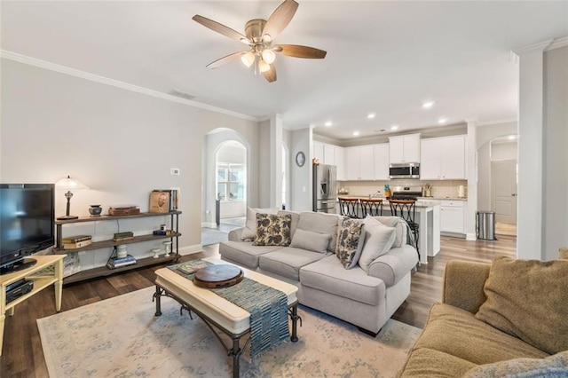 living room featuring ornamental molding, arched walkways, visible vents, a ceiling fan, and wood finished floors