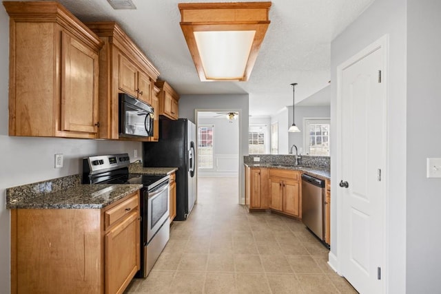 kitchen featuring black appliances, brown cabinetry, dark stone countertops, and a sink