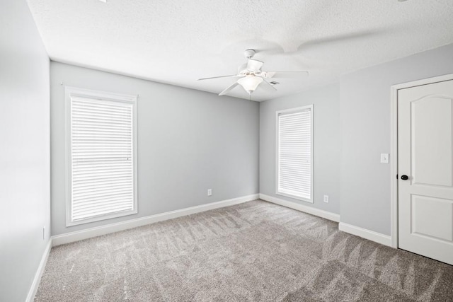 carpeted spare room with plenty of natural light, ceiling fan, baseboards, and a textured ceiling