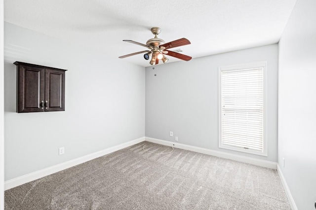 spare room with a healthy amount of sunlight, carpet, baseboards, and a ceiling fan