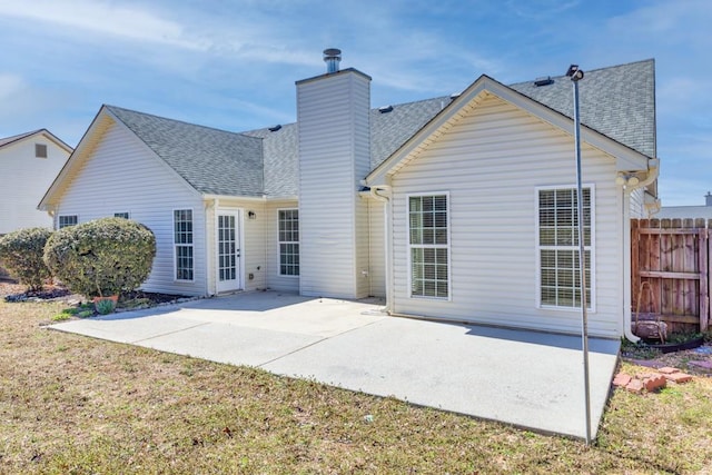 rear view of house with a shingled roof, fence, a chimney, and a patio