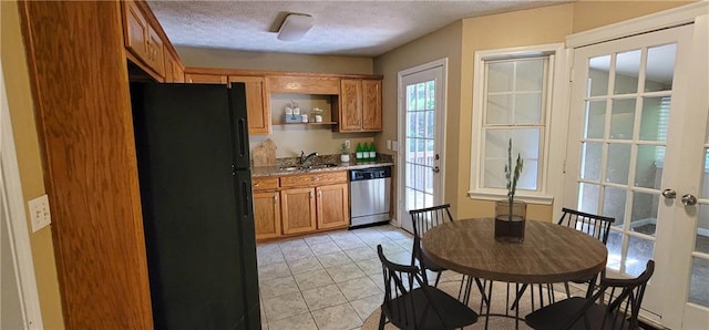 kitchen with black fridge, light tile patterned flooring, dishwasher, a textured ceiling, and sink